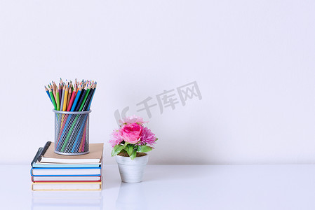 书架上的铅笔盒和白桌上的人造花盆