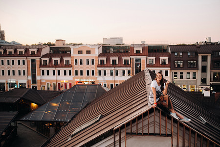 女孩坐在屋顶摄影照片_晚上，一个女孩坐在城市一所房子的屋顶上。