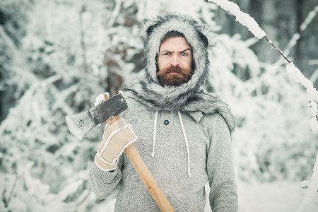 冬天留着胡须的伐木工人在白雪皑皑的冬季森林里拿着斧头。