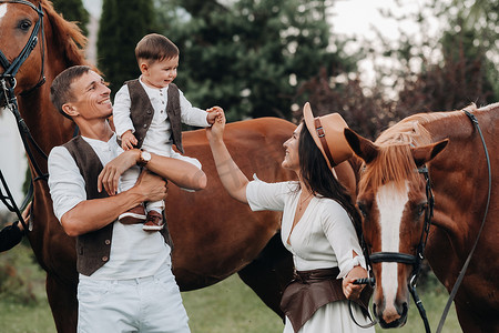 一个穿着白衣服的家庭和他们的儿子站在大自然中两匹美丽的马旁边。