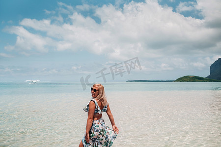 一个穿着泳衣的女孩站在海里，在毛里求斯岛莫纳山的背景下等待水上飞机。水中的女人回头看着一架降落在毛里求斯岛的飞机