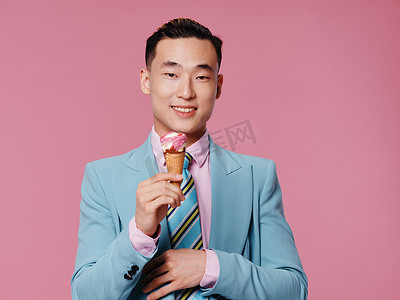 身穿蓝色西装、手拿冰淇淋的亚洲微笑男子情绪粉红色背景