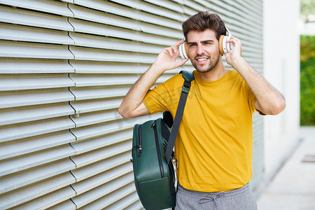 戴耳机的学生摄影照片_城市背景中戴耳机的年轻人