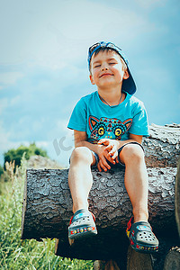 一个戴着棒球帽和短裤的孩子坐在一根木头上，梦想着什么