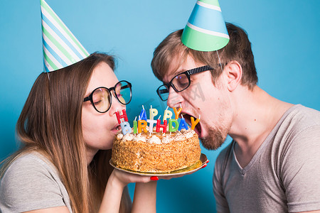 奇怪的年轻夫妇女孩和男孩戴着纸帽子的特写想要咬掉一块祝贺蛋糕。