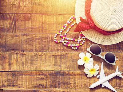 帽子、项链、太阳镜、花朵和红心形的平躺式作为暑假旅行的配饰，以及带有复制空间的木制背景平面模型。