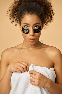 淋浴后裹着白毛巾的年轻女子的肖像，在米色背景下隔离的眼罩下涂上黑色