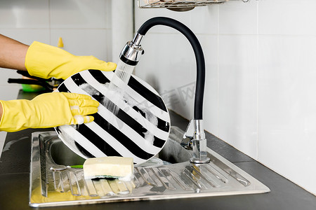 戴着黄色橡胶手套的人手在厨房水槽里洗碗。