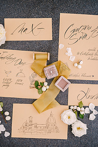 意大利佛罗伦萨 — 2019年10月3日：盒子里的结婚戒指、邀请卡、丝带、黑色背景的白玫瑰。