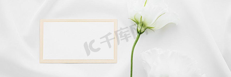 婚礼请柬或礼品卡和丝质织物上的白玫瑰花作为新娘平铺背景、白纸和假日品牌、平铺设计