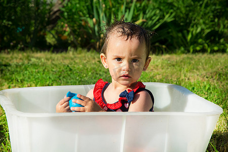 在炎热的夏日，一个非常严肃的一岁半女孩在白色浴缸里玩蓝色橡胶玩具