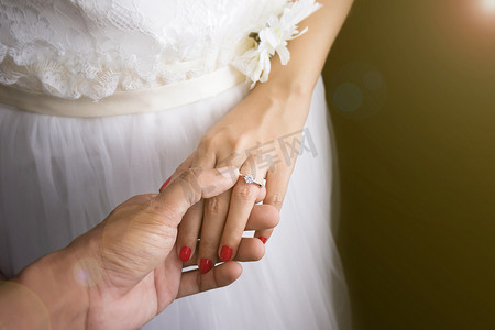 婚礼爱情情侣概念：新郎在婚礼当天将结婚戒指戴在新娘的手指上，日出效果与镜头光晕