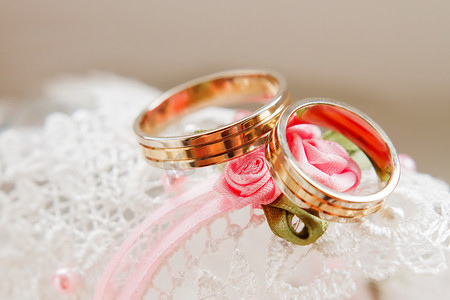金色婚礼装饰摄影照片_花边白色织物上的金色结婚戒指。