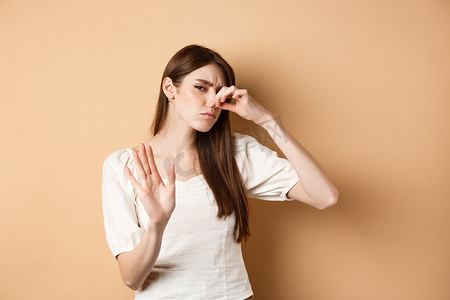 不高兴的女人因难闻的气味而堵住鼻子，表现出停止的手势，并因厌恶而皱眉。