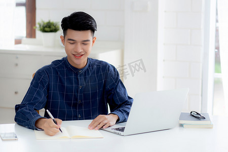 学习规划摄影照片_年轻的亚洲商人在笔记本上写作，规划工作，并在家里的办公桌上使用笔记本电脑，记录有关金融、男性学习、商业和沟通概念的笔记。