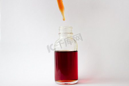 深吸摄影照片_一个玻璃瓶中的深红色液体，带有吸移管和白色背景上的一滴。