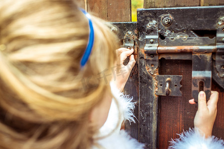 爱丽丝梦游仙境风景中一个美丽小女孩的侧视图，望着大门的钥匙孔