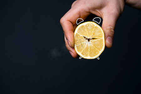 食物可爱风格摄影照片_一个男人的手拿着一个切好的柠檬，风格像闹钟。