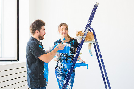 修理、翻新、宠物和情侣概念 — 带猫的年轻家庭一起修理和粉刷墙壁，笑着