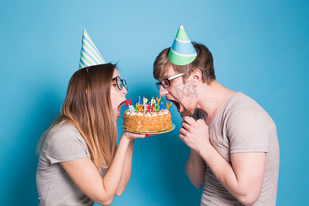 戴着纸帽子的奇怪的年轻夫妇女孩和男孩想咬掉一块祝贺蛋糕。