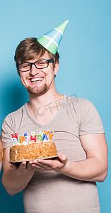戴着问候纸帽子的滑稽疯狂的年轻人想要咬掉一块祝贺蛋糕。