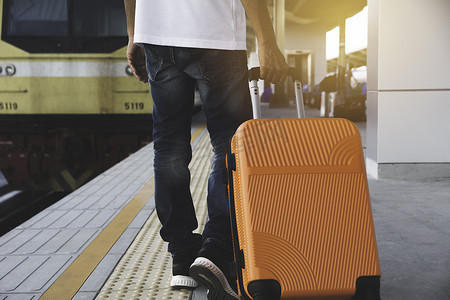 拖着行李旅行摄影照片_男子拖着橙色手提箱行李袋，走在火车站