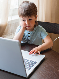 好奇的蹒跚学步的男孩探索笔记本电脑并按下电脑键盘上的按钮。