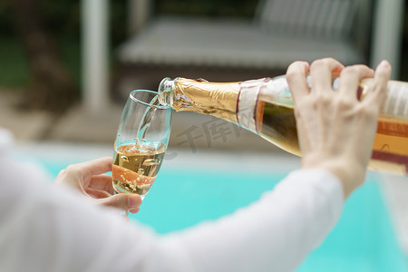 欢庆庆祝摄影照片_女人的手将香槟倒入玻璃杯中。