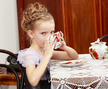 可爱的小女孩在旧桌子上喝茶。