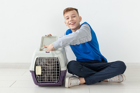 猫地板摄影照片_在新公寓的地板上，笑得积极的小男孩拿着一个笼子，旁边有一只苏格兰折耳猫。