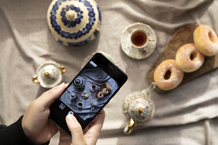 卡台面摄影照片_女士、博客作者坐在咖啡馆里，用食物手机拍照、桌上有甜甜圈和马卡龙的下午茶高角度、食物和社交媒体概念的顶视图图片