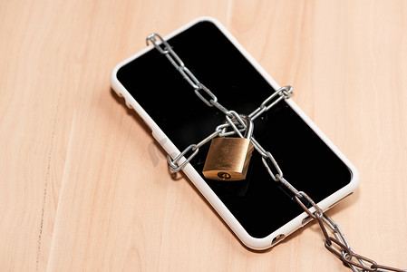 智能手机在木桌上绑着带锁的链子。