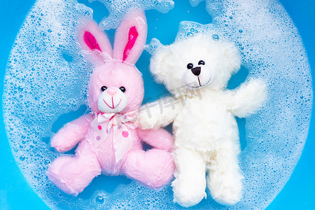 将带玩具泰迪熊的兔子娃娃浸泡在洗衣粉水中