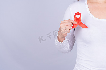女性胸前挂着红色艾滋病意识丝带，并举起手在灰色背景下与他们作斗争。