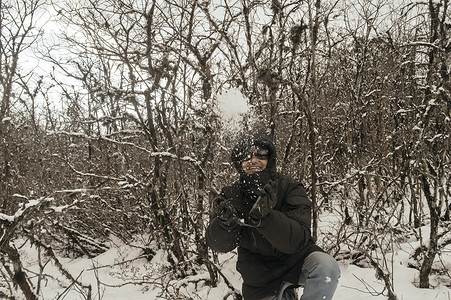 夏天雪山摄影照片_一个穿着黑色套头夹克的男人微笑着快乐地享受着第一场雪的玩耍和向空中扔雪球的肖像。
