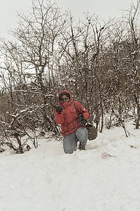 一个穿着红色套头夹克的女人微笑着快乐地享受着第一场雪的玩耍和向空中扔雪球的肖像。