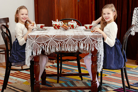 可爱的小杯子摄影照片_女孩双胞胎在一张配有蕾丝桌的古董桌上喝茶