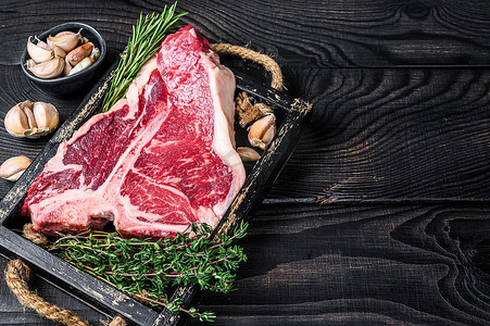 上等腰肉牛排或 T 骨生牛肉牛排配香草和盐在木托盘中。