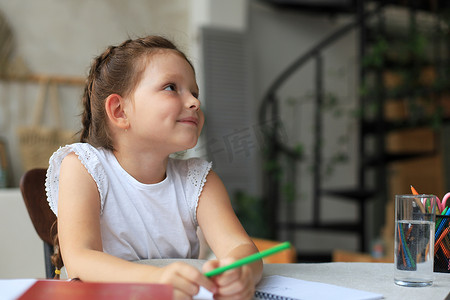 小孩子写字摄影照片_小女孩坐在书桌前，在笔记本上写字，在家做练习，小孩子手写准备作业。