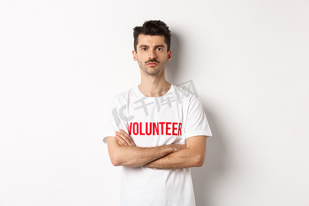 身穿白色T恤的严肃的年轻男性志愿者，双臂交叉在胸前，看着镜头，准备提供帮助