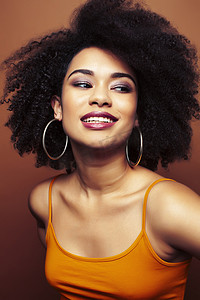 漂亮的年轻非洲裔美国女性，一头卷发，在棕色背景下摆出欢快的手势，人们的生活方式观念