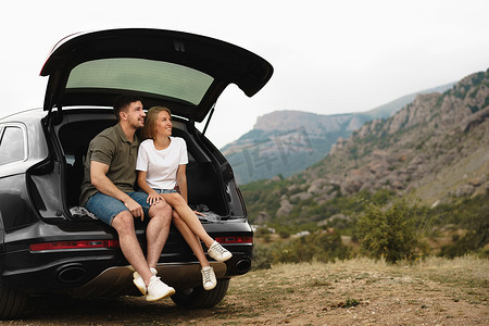 年轻快乐的夫妇坐在汽车后备箱里进行公路旅行