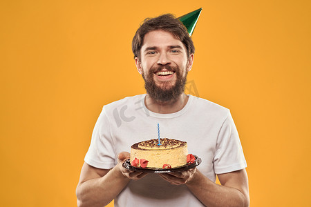 英文版生日快乐摄影照片_戴着帽子的生日男孩，带着蛋糕有趣的黄色背景派对