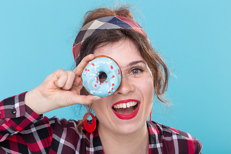 一位美丽微笑的年轻女子的特写肖像，她的眼睛上有一个蓝色的甜甜圈，摆在蓝色背景上。