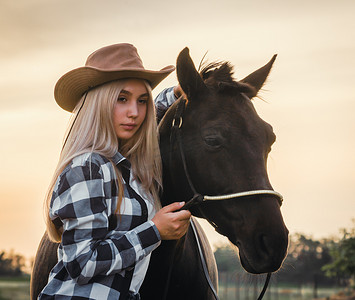 带着牛仔帽摄影照片_戴着牛仔帽和带马的格子衬衫的年轻女孩