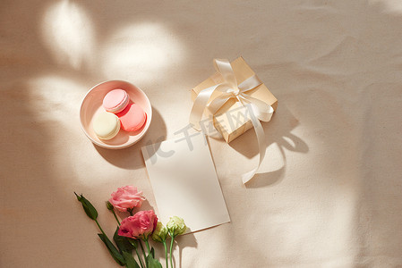 浅色背景下的空白纸条、牛皮纸信封、礼品盒、织物和鲜花的顶视图