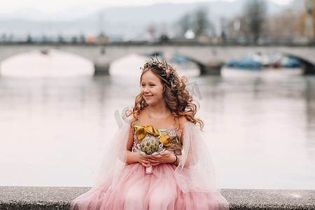 粉色裙摄影照片_一个穿着粉色公主裙、手里拿着花束的小女孩走过苏黎世老城。瑞士城市街道上一个穿着粉色裙子的女孩的肖像