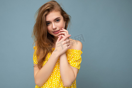 可爱的年轻迷人的深色金发女郎，有着真诚的情感，隔离在背景墙上，有复制空间，穿着时尚的夏季黄色连衣裙。