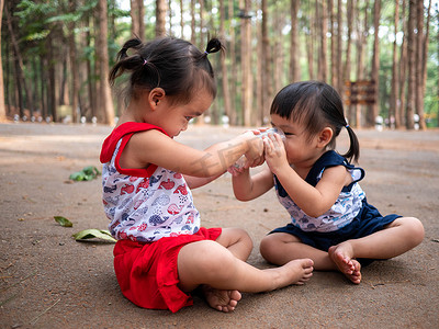 亚洲小孩坐在花园里，用玻璃杯给姐姐喂牛奶