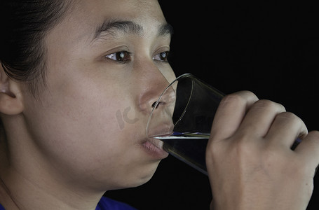 亚洲年轻女子在黑色背景下喝透明玻璃中的凉水。